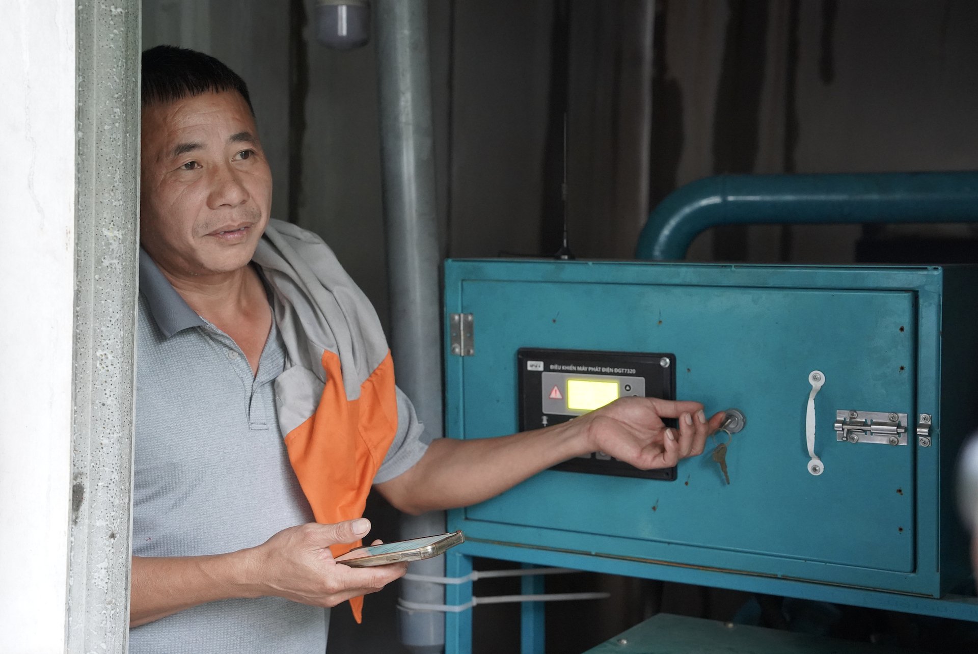 Ông Trần Xuân Phong, chủ trang trại, sử dụng điện thoại thông minh để khởi động máy phát điện chạy bằng khí sinh học (biogas). Ảnh: Phương Linh.