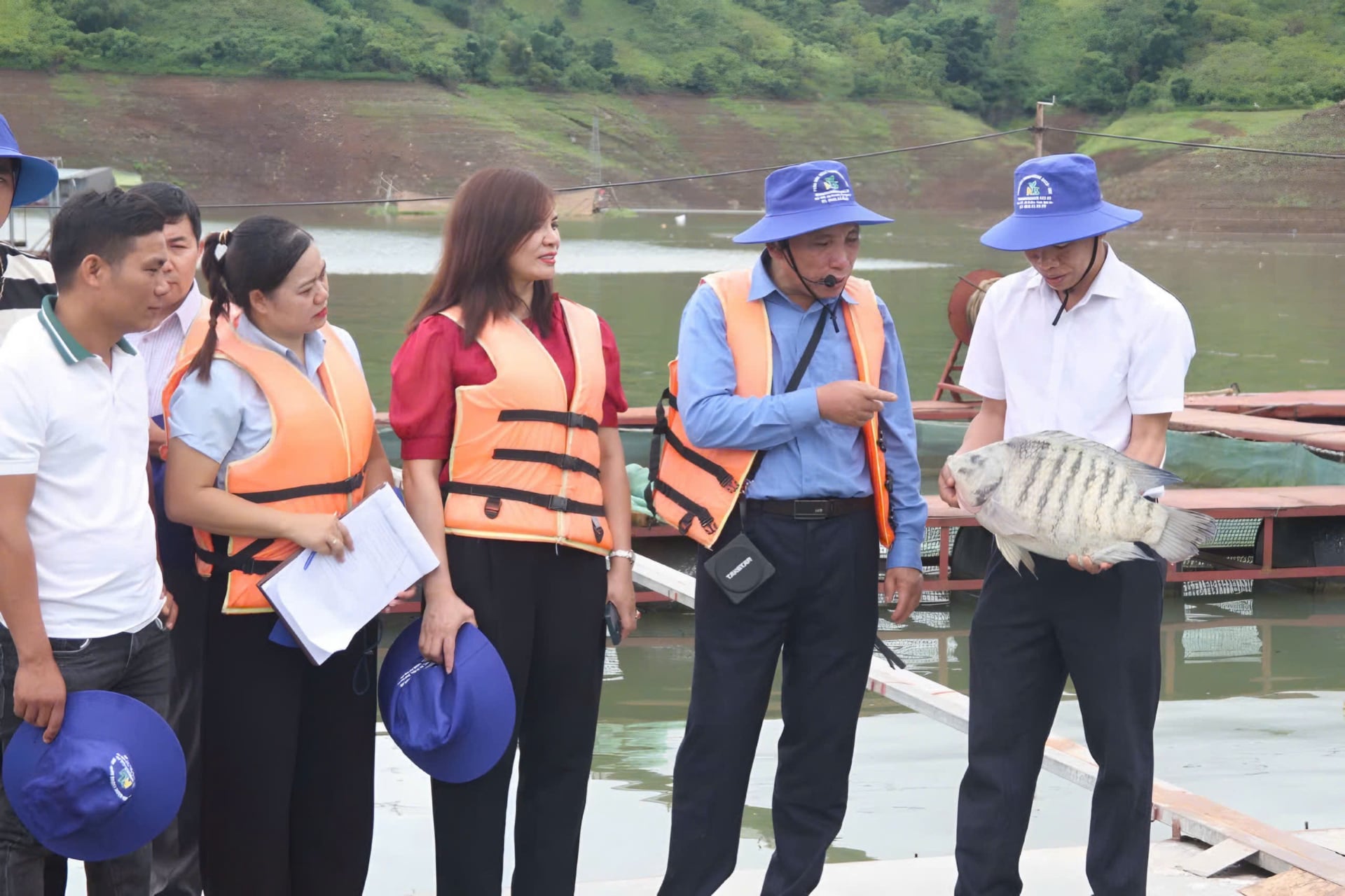 Ông Phạm Văn Doanh (thứ 2 từ phải sang) giới thiệu mô hình nuôi cá thương phẩm trên lòng hồ thủy điện. Ảnh: Nguyễn Nga.
